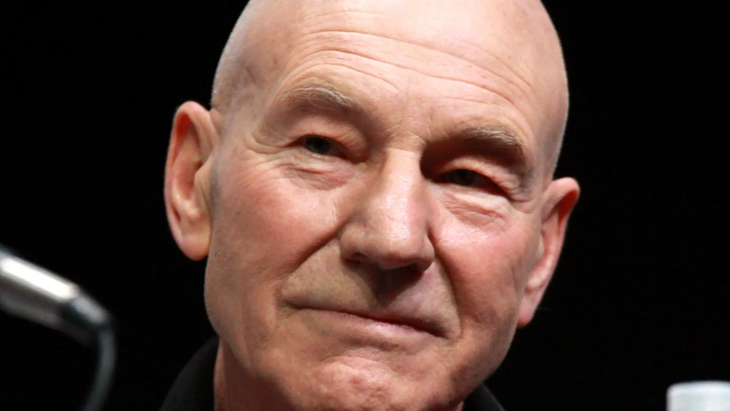 Patrick Stewart, who died at 86, smiling at a convention panel microphone in a file photo