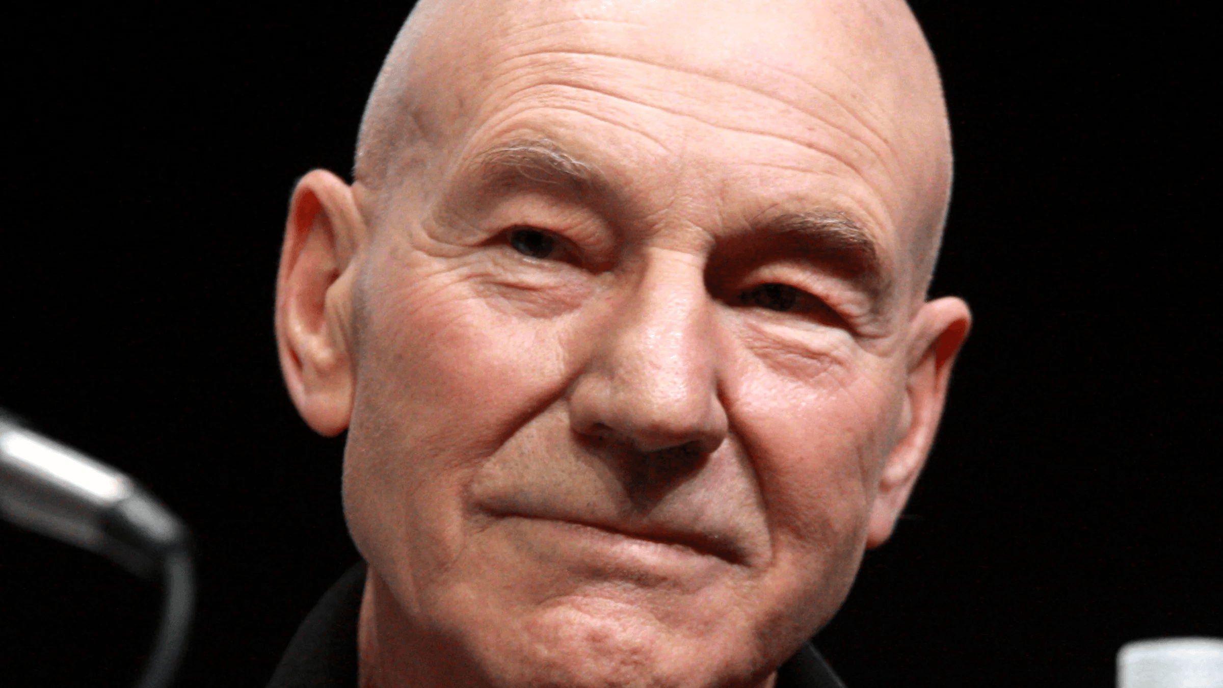 Patrick Stewart, who died at 86, smiling at a convention panel microphone in a file photo
